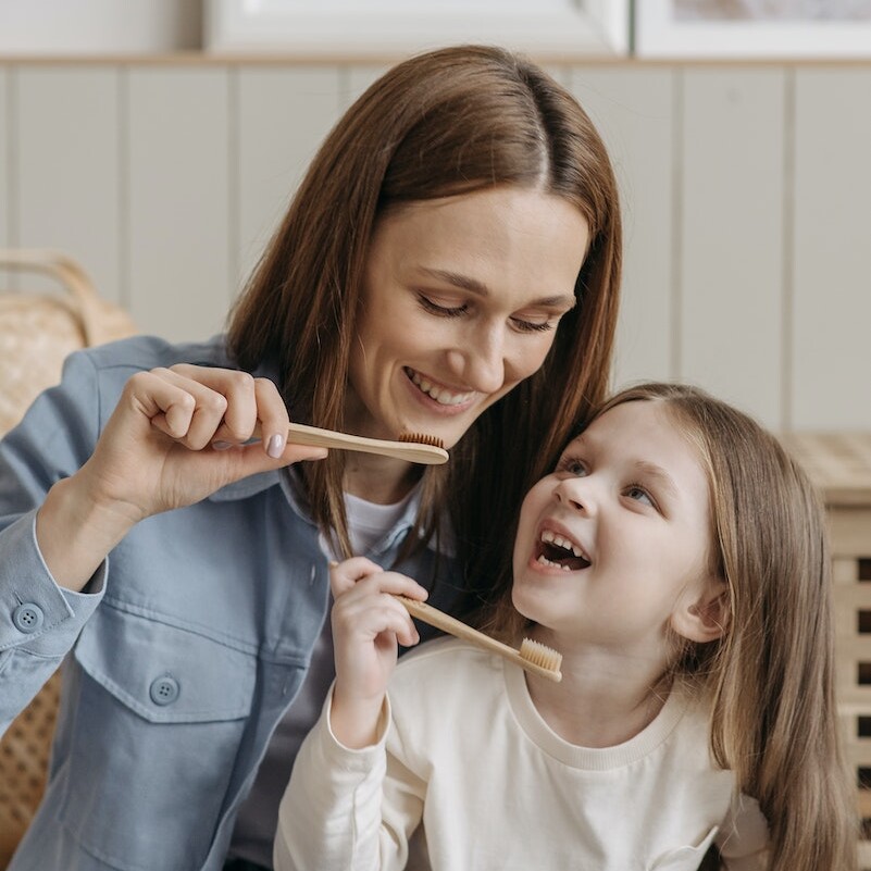 Photo of a Kid and Her Mother Holding Wooden Toothbrushes